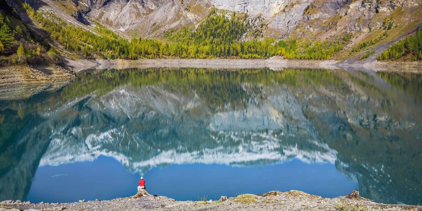 Mann am Lac de Tseuzier im Wallis mit Blick auf Bergspiegelung und verschneite Gipfel der Region Crans Montana