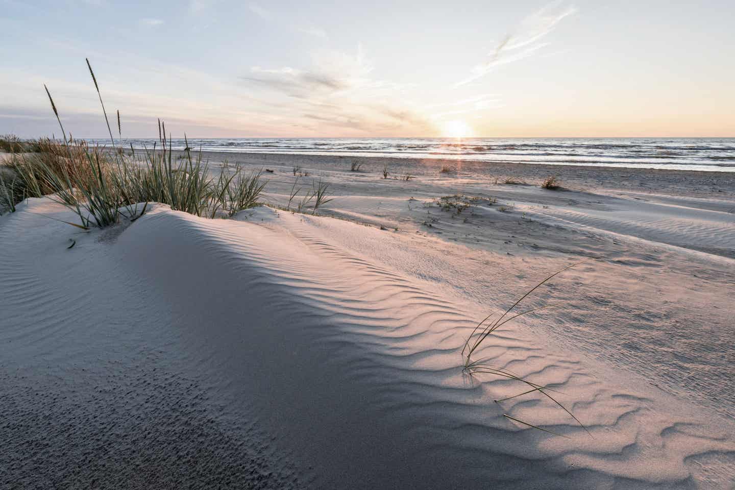 Blick über die Dünen eines Ostseestrand in Lettland, im Hintergrund das Meer und die untergehende Sonne