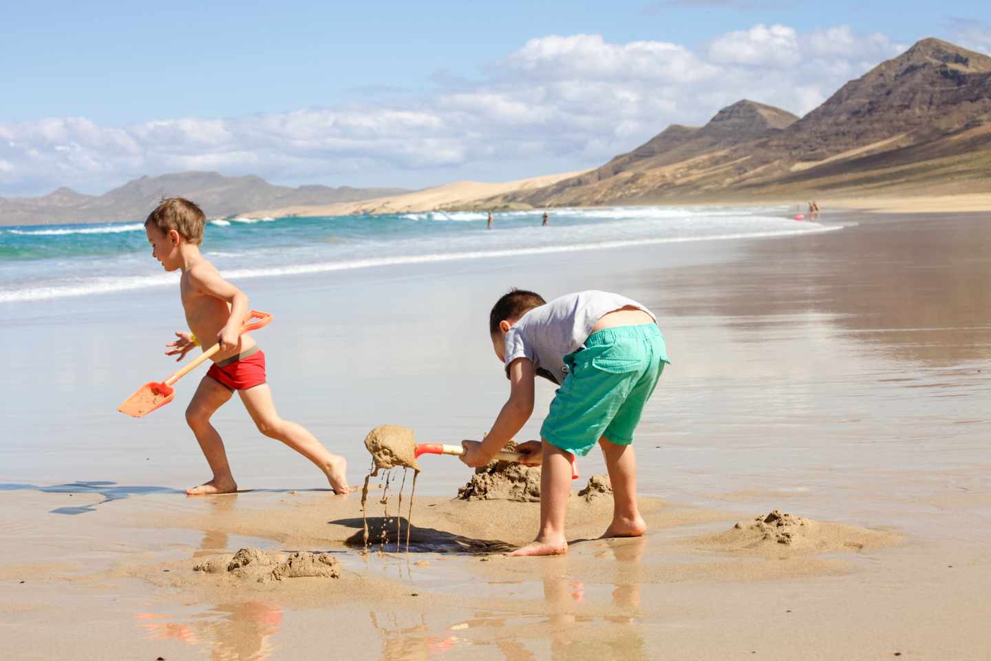 Zwei Kinder buddeln mit Schaufeln im Sand am Strand von Fuerteventura, Kanaren, Spanien
