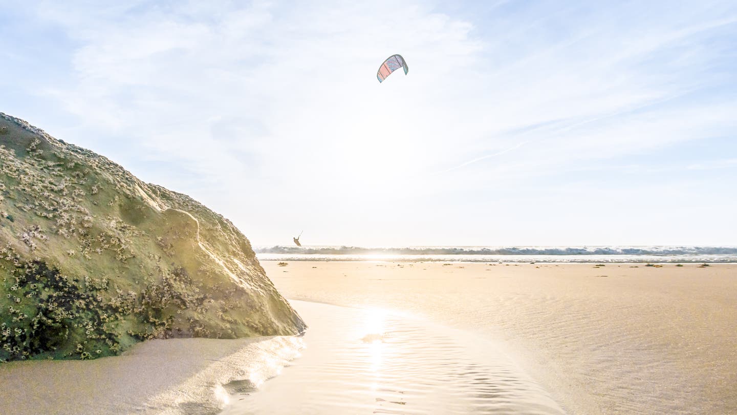 Kitesurfer bei Sonnenuntergang am Strand von Tarifa, Andalusien, mit Blick über Meer und Felsen