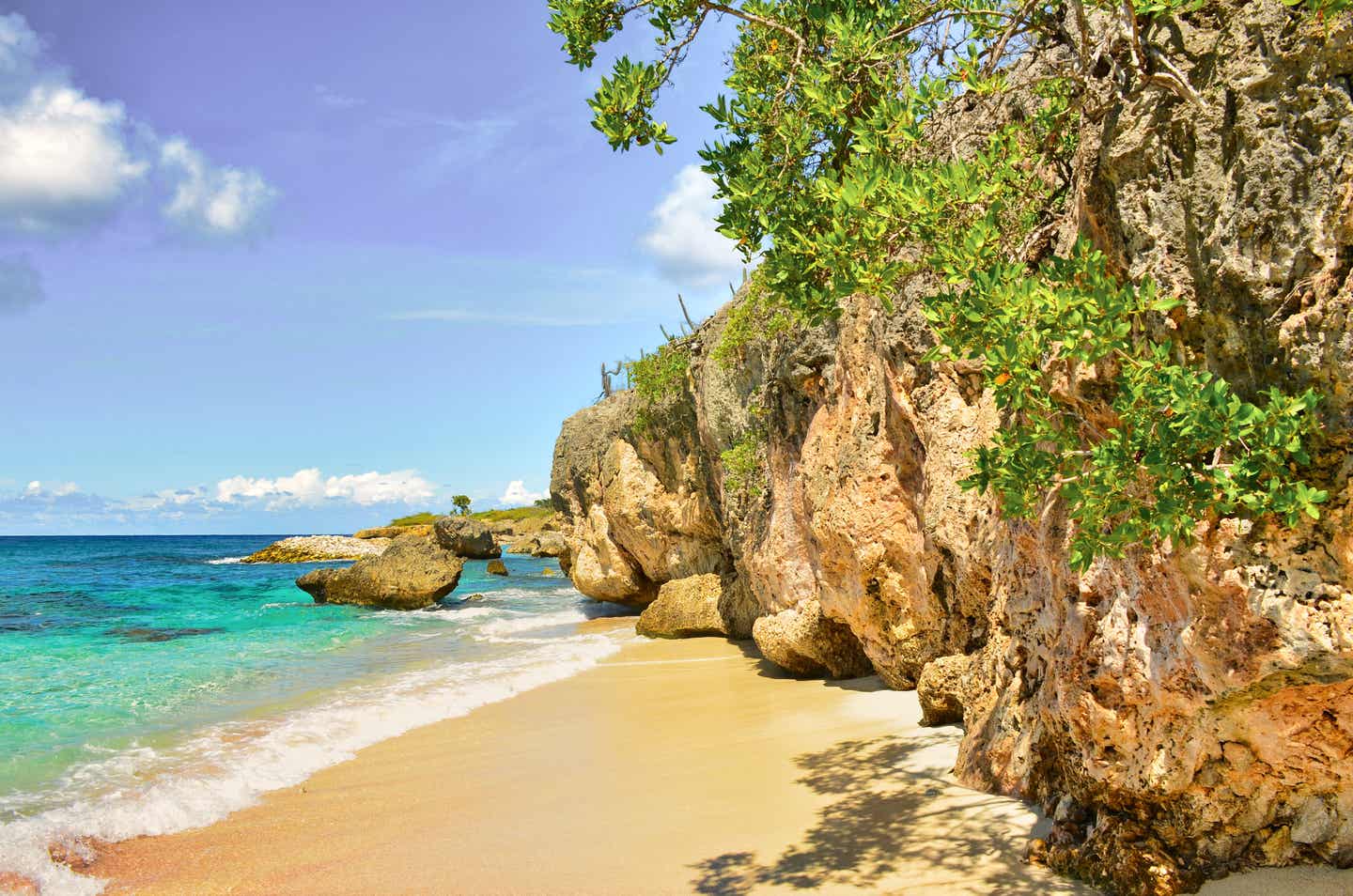Goldener Sand und blaues Wasser vor braunen Felsen auf Bonaire