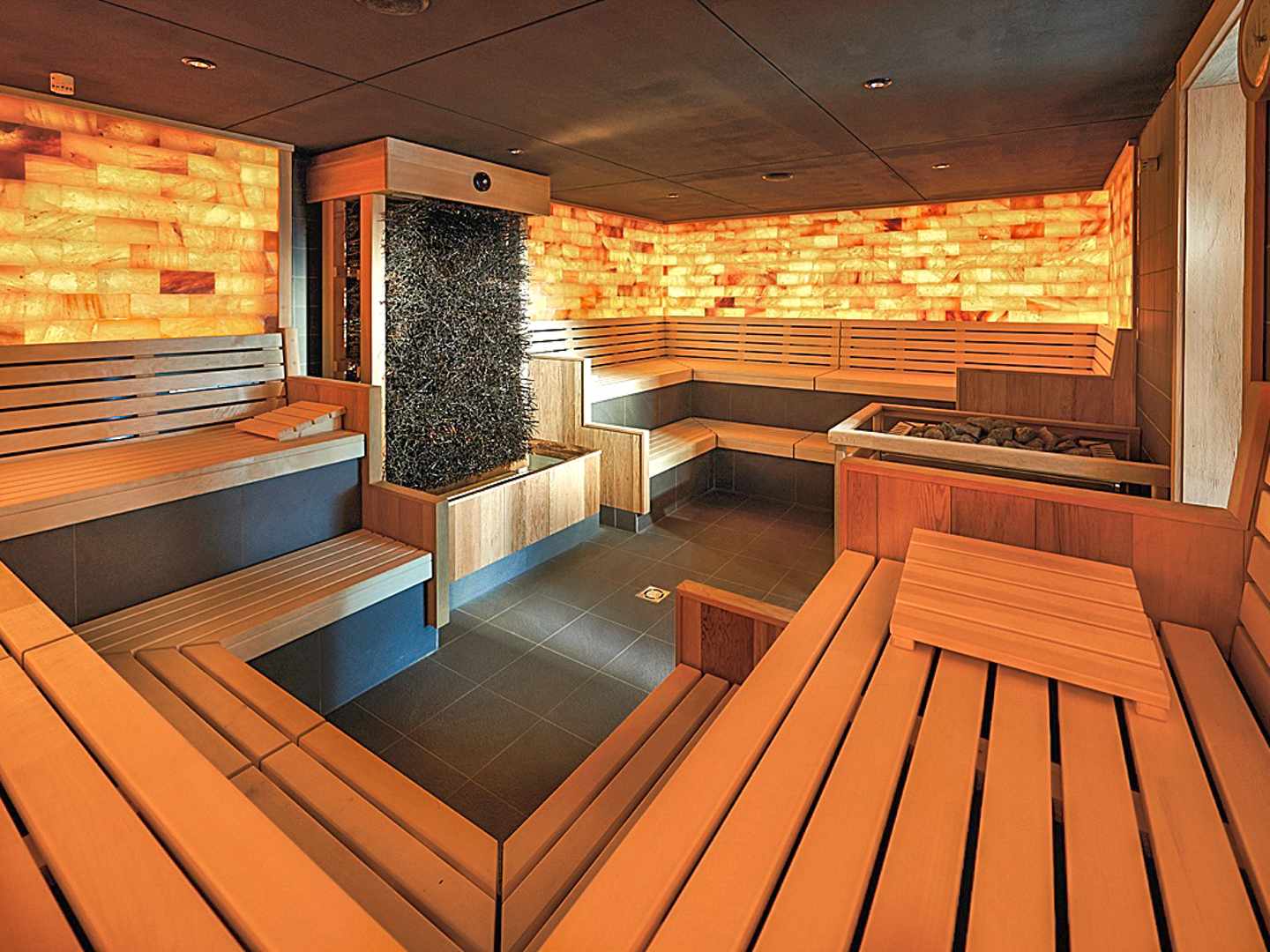 Sauna mit Salzsteinwand und klarer Struktur – verschiedene Sitzhöhen ermöglichen unterschiedliche Temperaturzonen Saunabereich im bora HotSpaResort Radolfzell mit Holzliegen und beleuchteter Salzsteinwand
