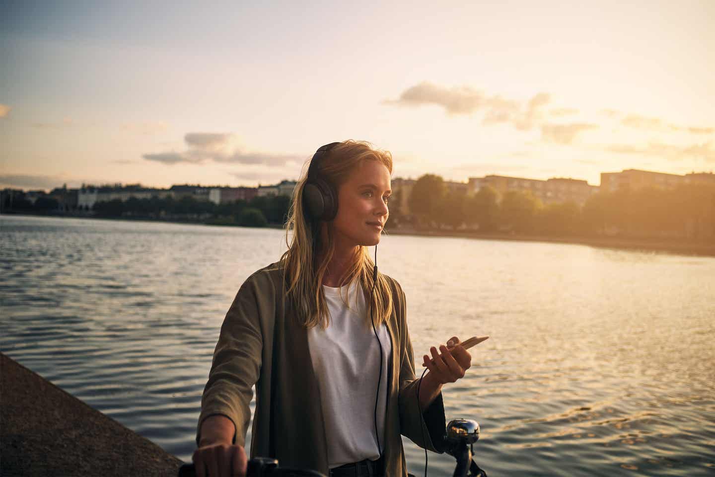 Eine Frau trägt Kopfhörer am See während eines Sonnenuntergangs