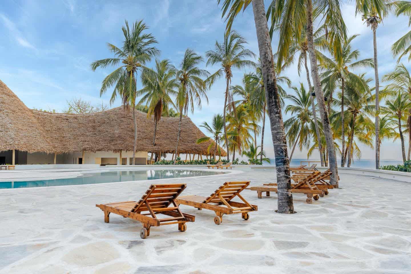 Poolbereich im ananea Diamonds Malindi mit Holzliegen, Palmen und traditionellem Makuti-Dach direkt an der Küste Kenias