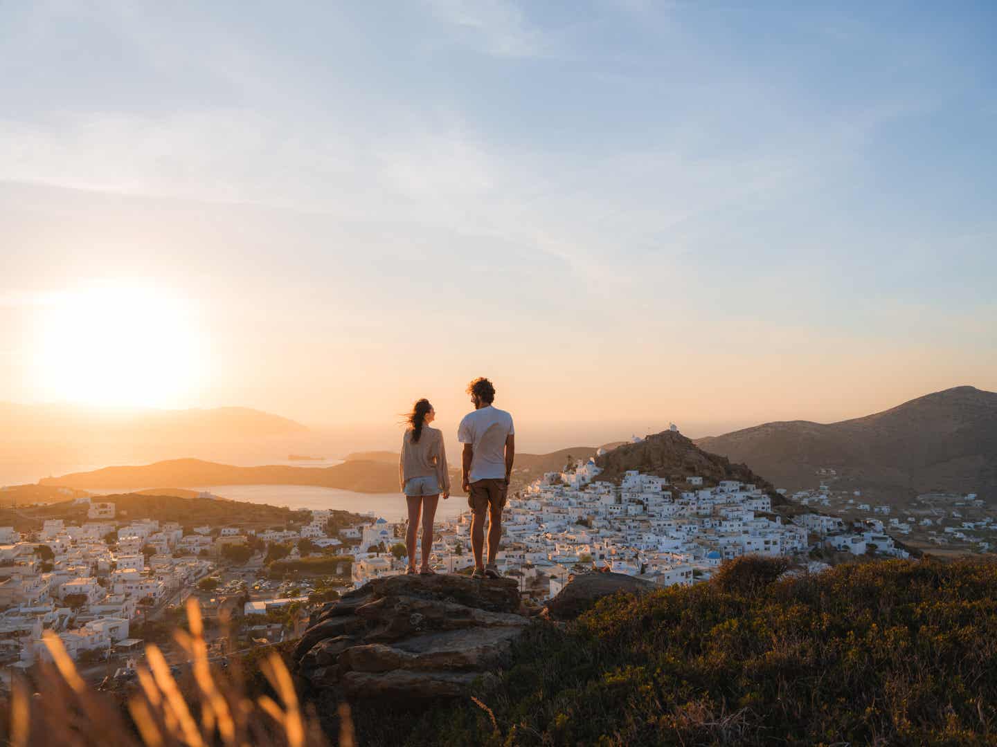 Junges Paar genießt auf einem Dach in Santorini den weiten Blick über die Ägäis und die ikonischen weißen Häuser mit blauen Kuppeln