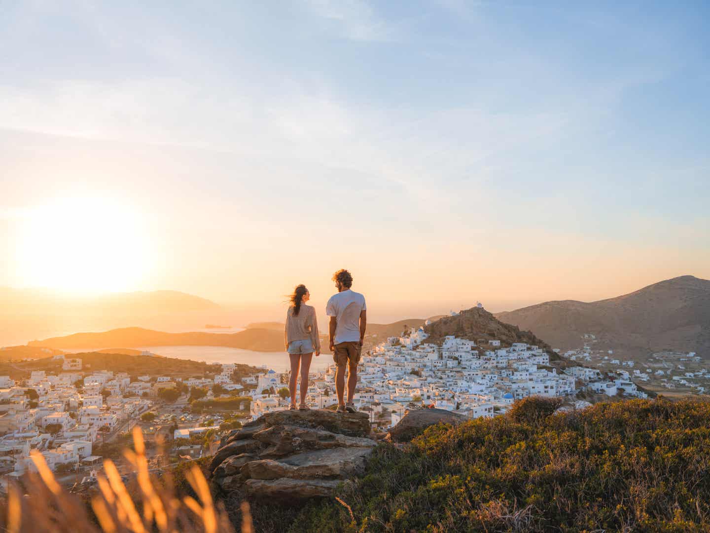 Junges Paar genießt auf einem Dach in Santorini den weiten Blick über die Ägäis und die ikonischen weißen Häuser mit blauen Kuppeln