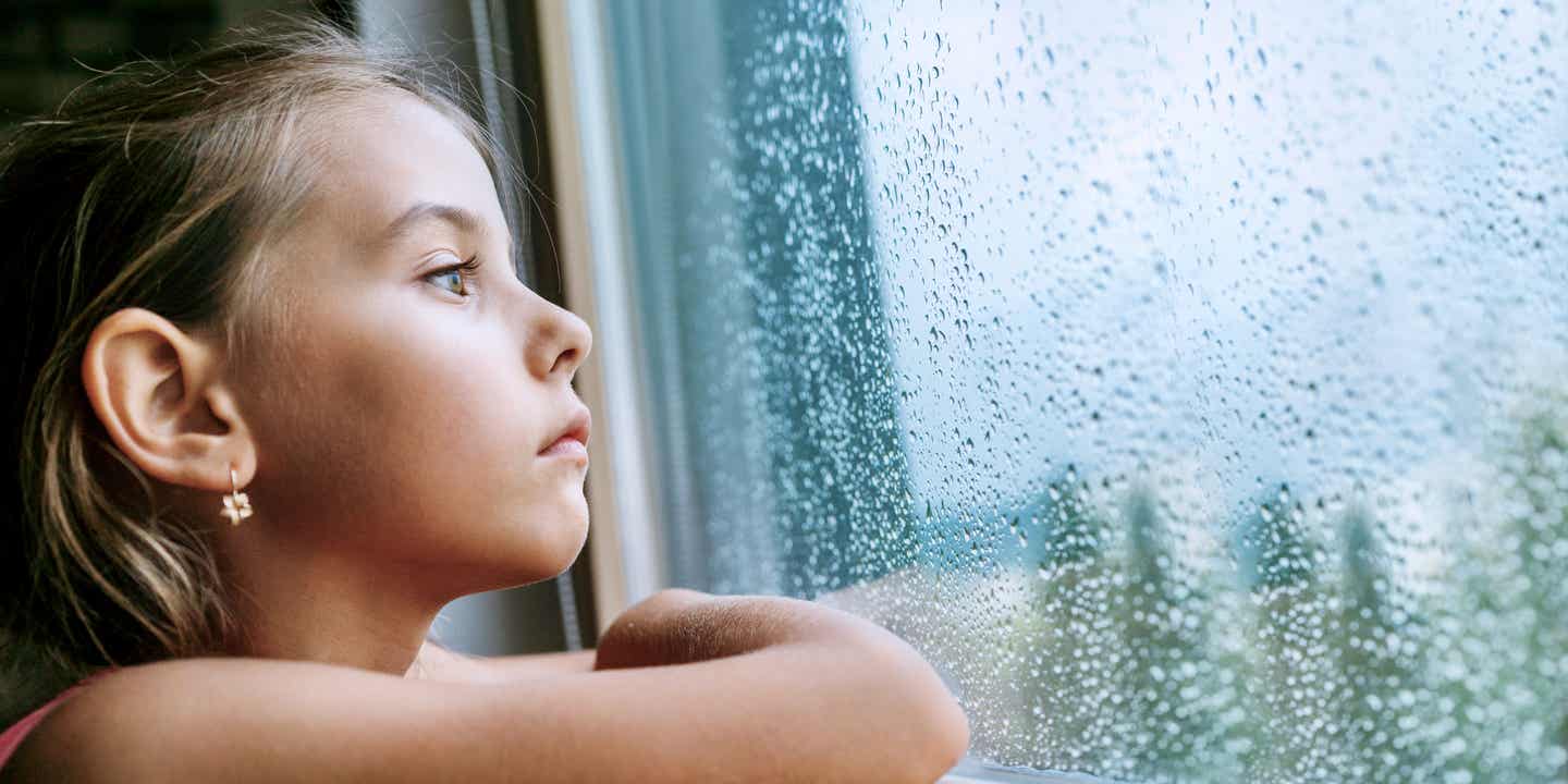 Ein Kind schaut traurig aus dem vollgeregneten Fenster