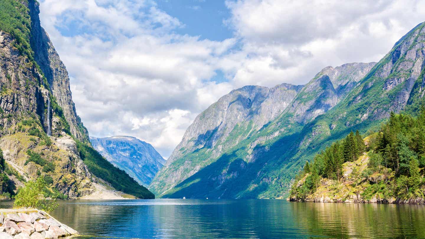 Naeroyfjord in Norwegen – klare Gewässer, steile Berge und Wasserfall bei bewölktem Himmel. Fjorde Norwegen in voller Pracht