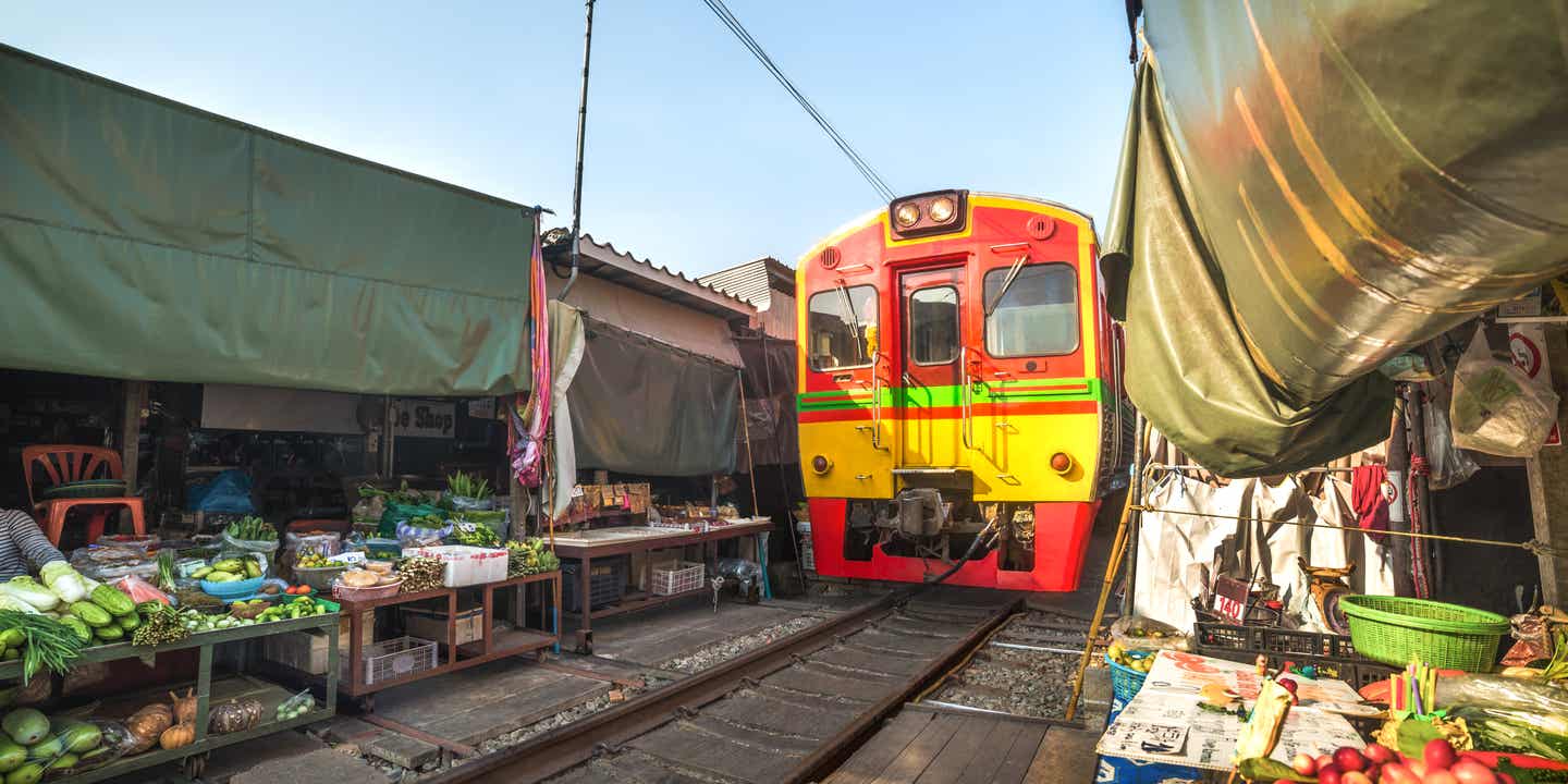 Regenschirmmarkt auf der Eisenbahnstrecke an einem sonnigen Tag: der Zug fährt direkt durch den Markt