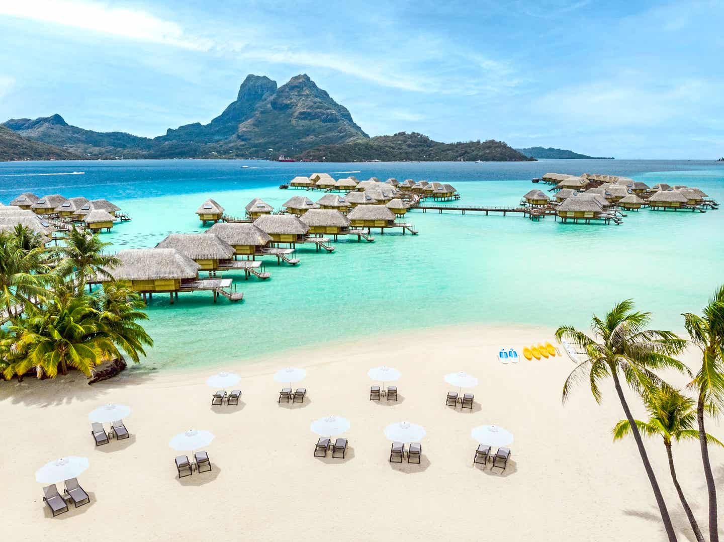 Blick auf ein Resort auf Bora Bora mit Hütten über dem Wasser und einem Berg im Hintergrund