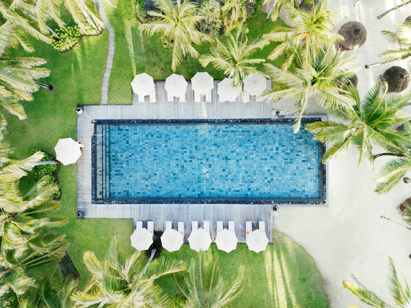 Einer der Hotelpools zwischen Palmen von einer Drohne aufgenommen