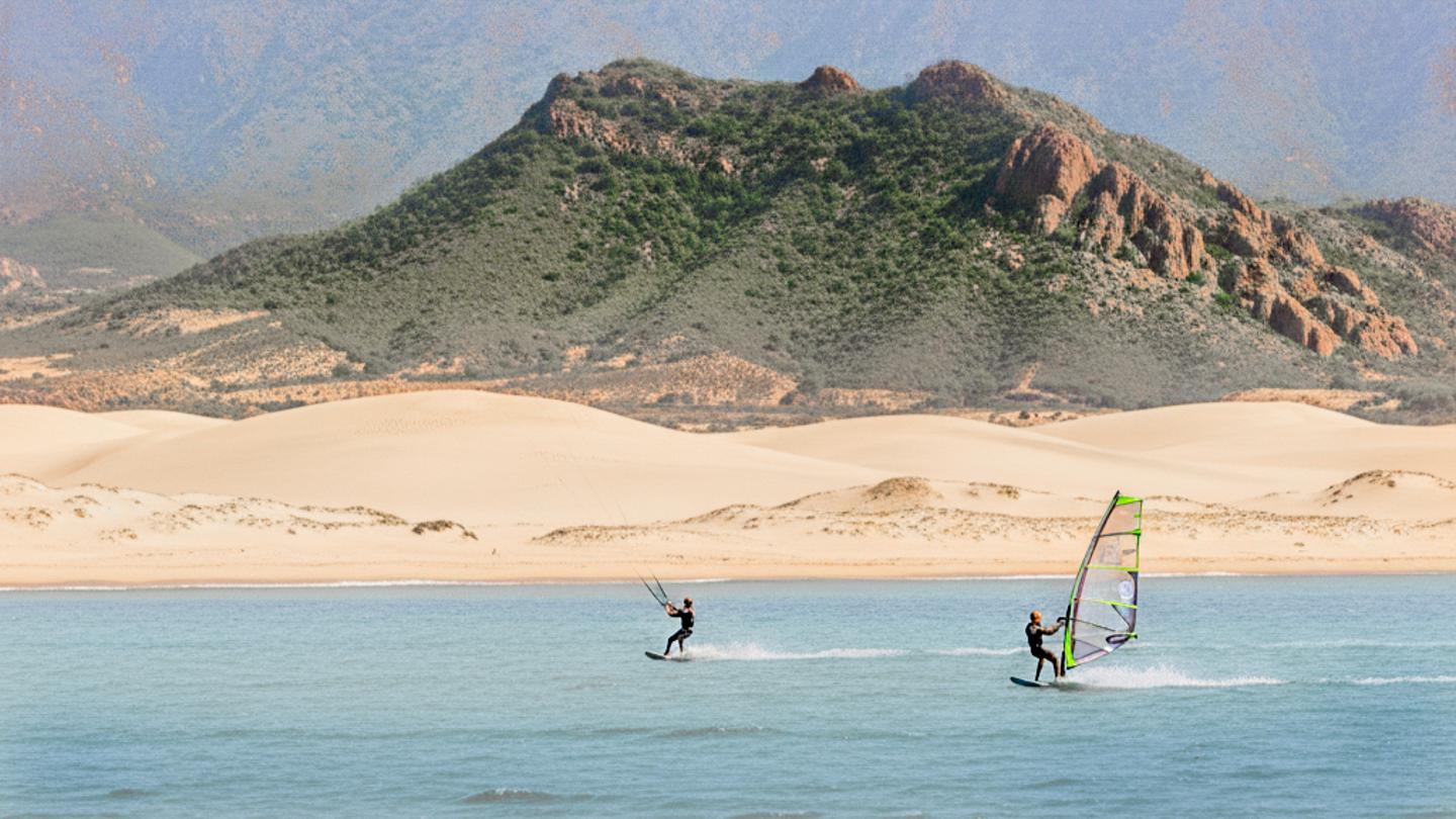 Surfen in Tarifa: Kite- und Windsurfern vor den Dünen und grünen Hügeln an der Costa de la Luz
