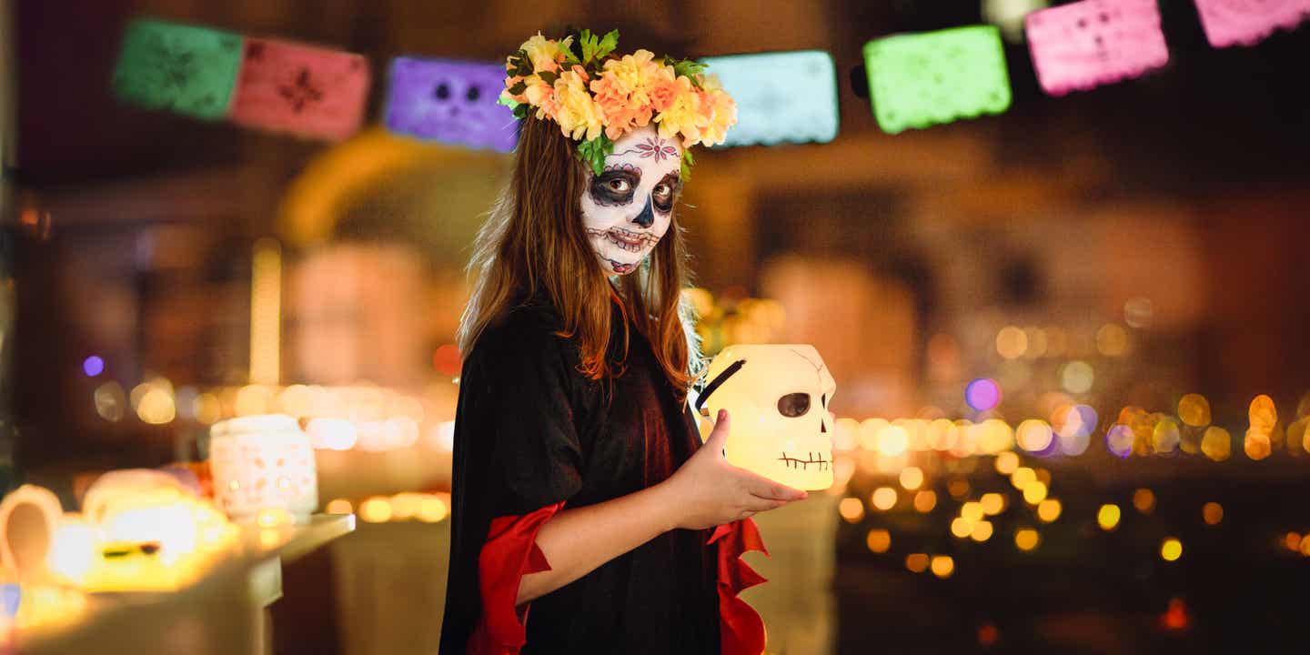 Mädchen für den Día de los Muertos geschminkt mit beleuchtetem Totenschädel in der Hand