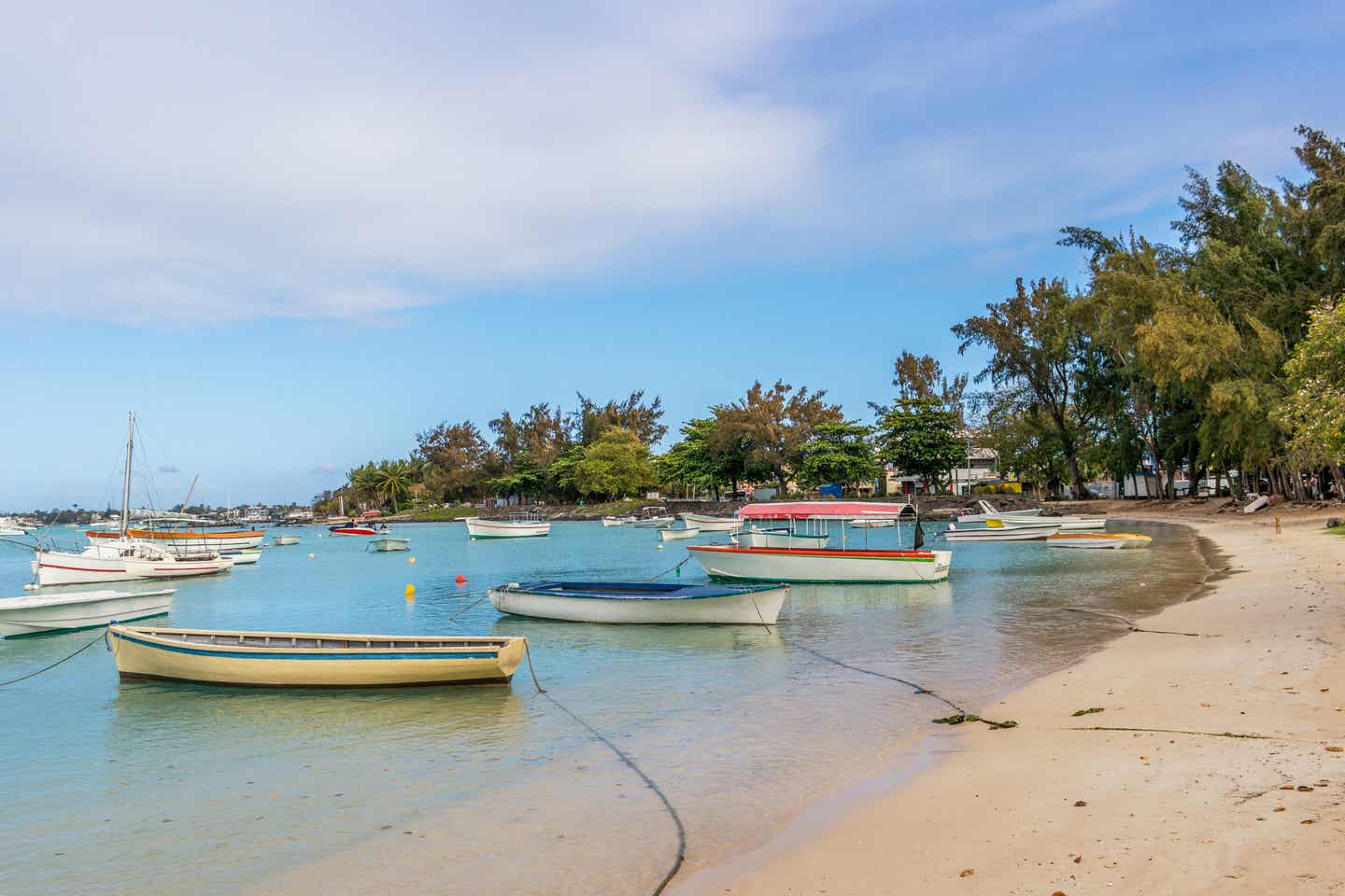 Viele im glasklaren Wasser des Grand Bai Public Beach anlegende Fischerboote, im Hintergrund von dicht bewachsenen Bäumen umrahmt