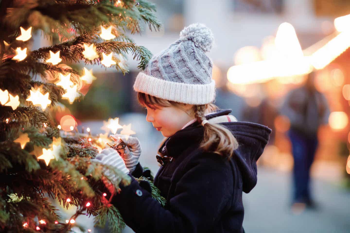 Kind mit Mütze vor Baum mit Lichtern