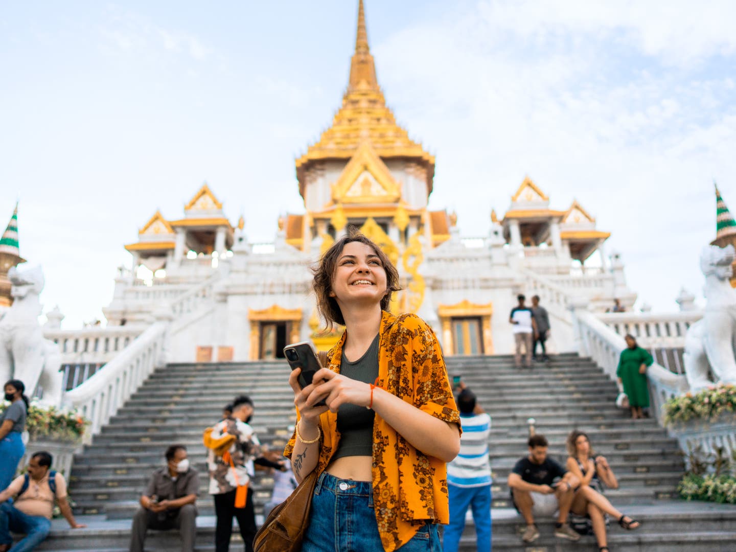 Junge Frau mit Smartphone vor dem Tempel Wat Traimit in Bangkok