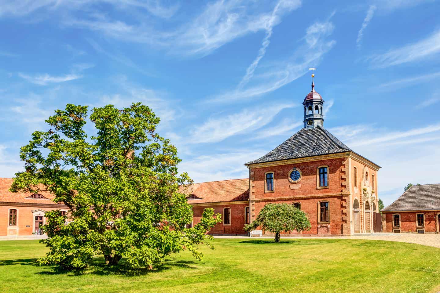 Weitläufige Rasenfläche mit großer Kastanie vor dem roten Backsteinbau von Schloss Bothmer mit Turm und blauem Himmel