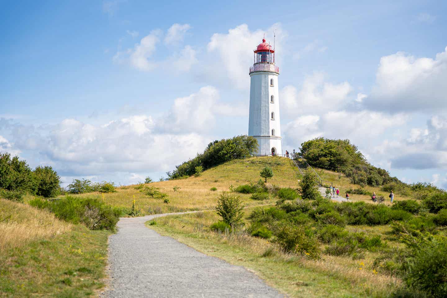 Leuchtturm Dornbusch auf der Insel Hiddensee, umgeben von grüner Natur und unter einem blauen Himmel mit Wolken.