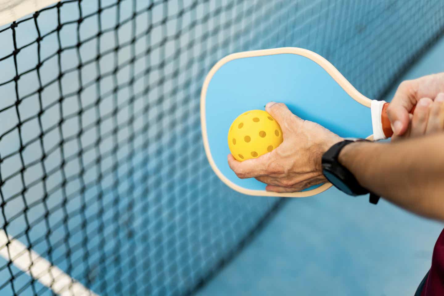 Mann hält einen türkisfarbenen Schläger und einen löchrigen gelben Pickleball-Ball