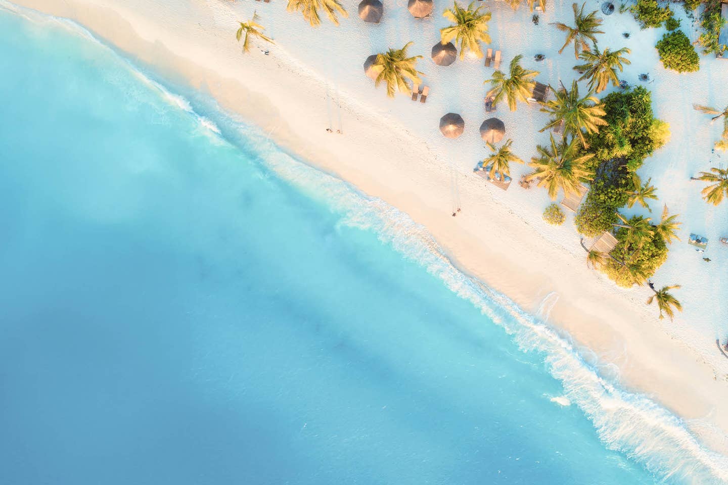 Türkisblaues Wasser, weißer Sandstrand mit Sonnenschirmen und Palmen von oben, Sansibar