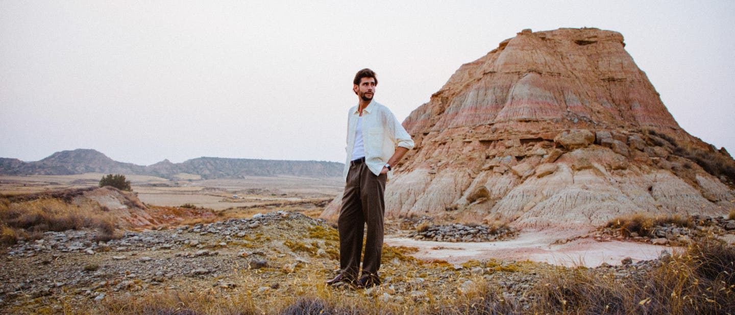 Alvaro Soler steht in einer Steppenlandschaft vor einem rötlich gefärbten Hügel