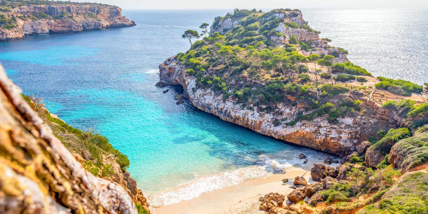 Bucht Caló des Moro auf Mallorca mit hellem Sandstrand, klarem Wasser und Felsklippen mit Pinienbewuchs