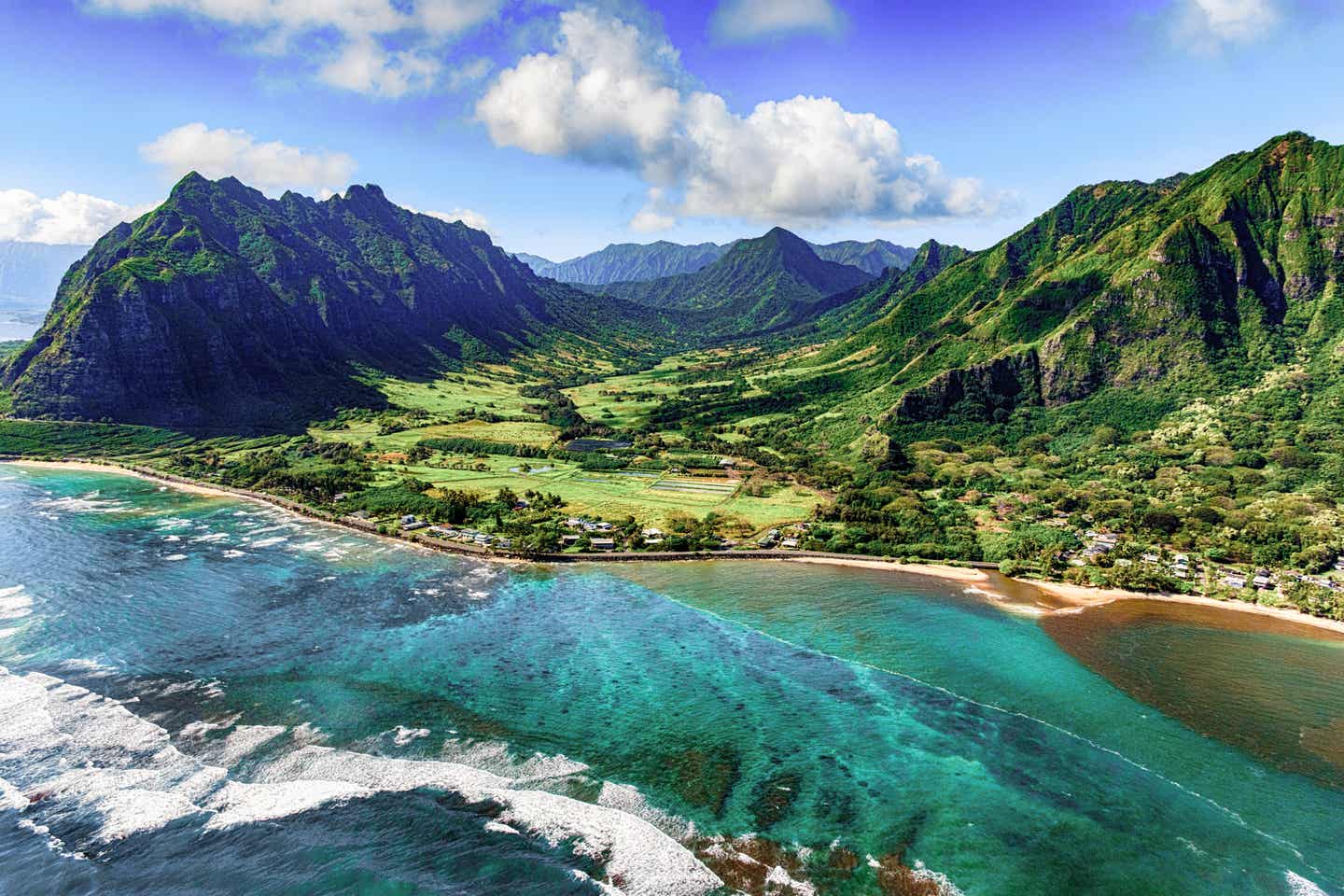 Der Kualoa Strand auf Hawaii mit türkisblauem Wasser inmitten üppig grüner Natur mit Bergen im Hintergrund