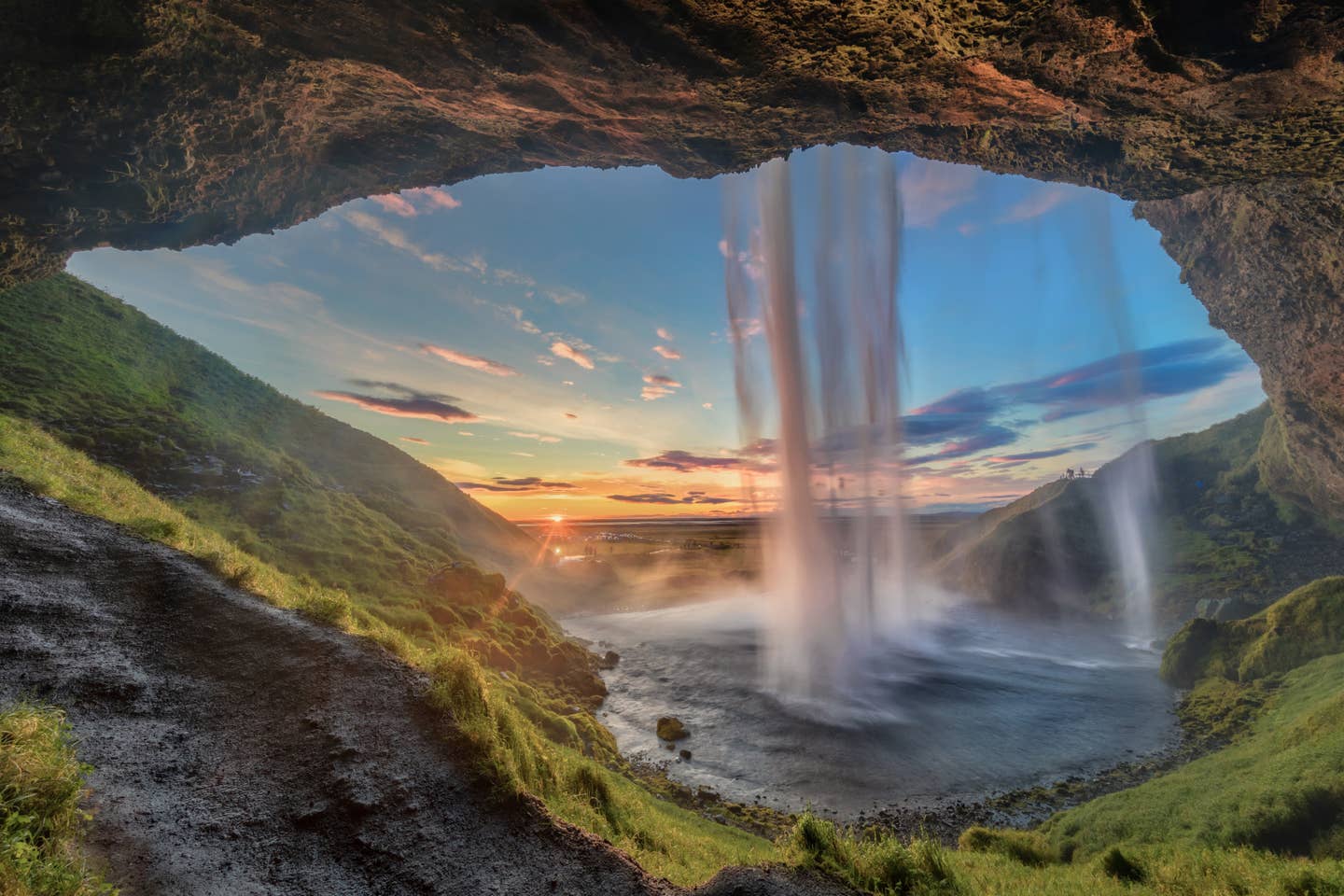 Island Urlaub mit DERTOUR. Der Seljalandsfoss-Wasserfall auf Island bei Sonnenuntergang von unterhalb des Falls aufgenommen