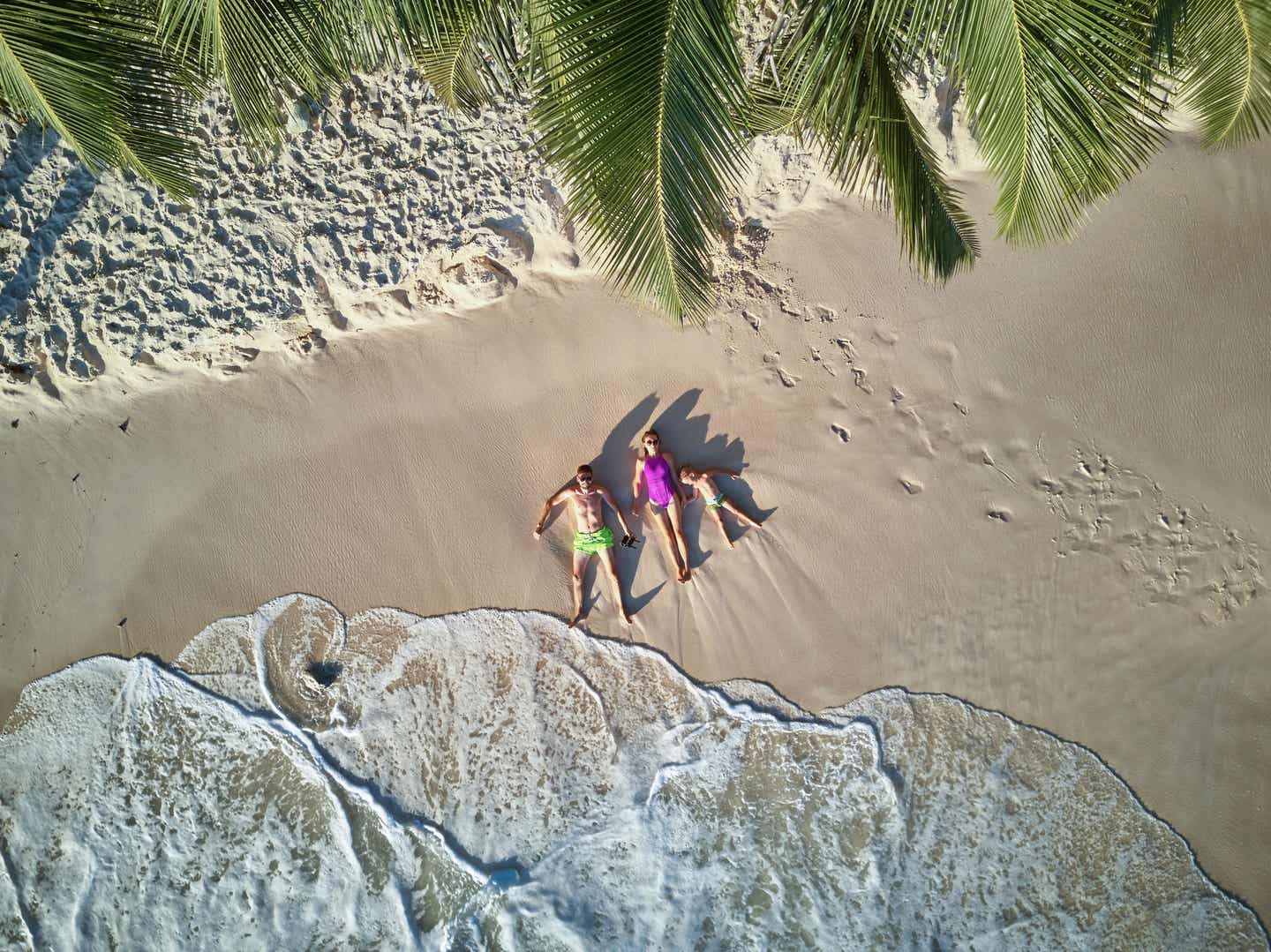 Eine Familie liegt im La-Digue-Urlaub am Strand und wird von sanften Wellen umspült