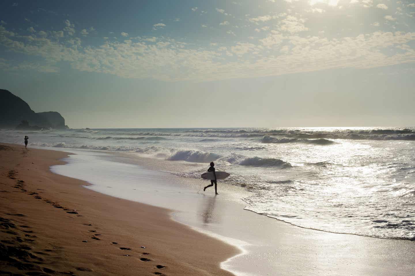 Portugal Urlaub mit DERTOUR. Surfer am Strand der Algarve auf dem Weg in die Wellen