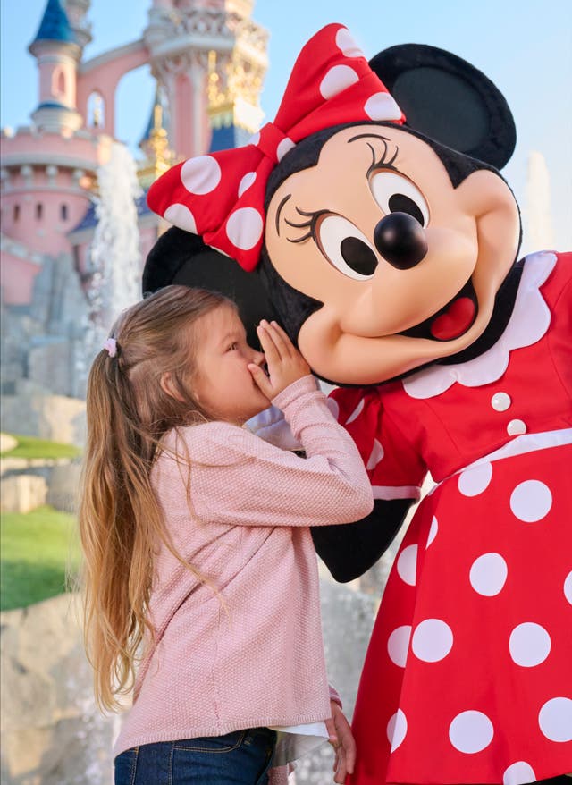 Jetzt entdecken Kind flüstert etwas in Ohr von Minnie Mouse, Disney Schloss im Hintergrund