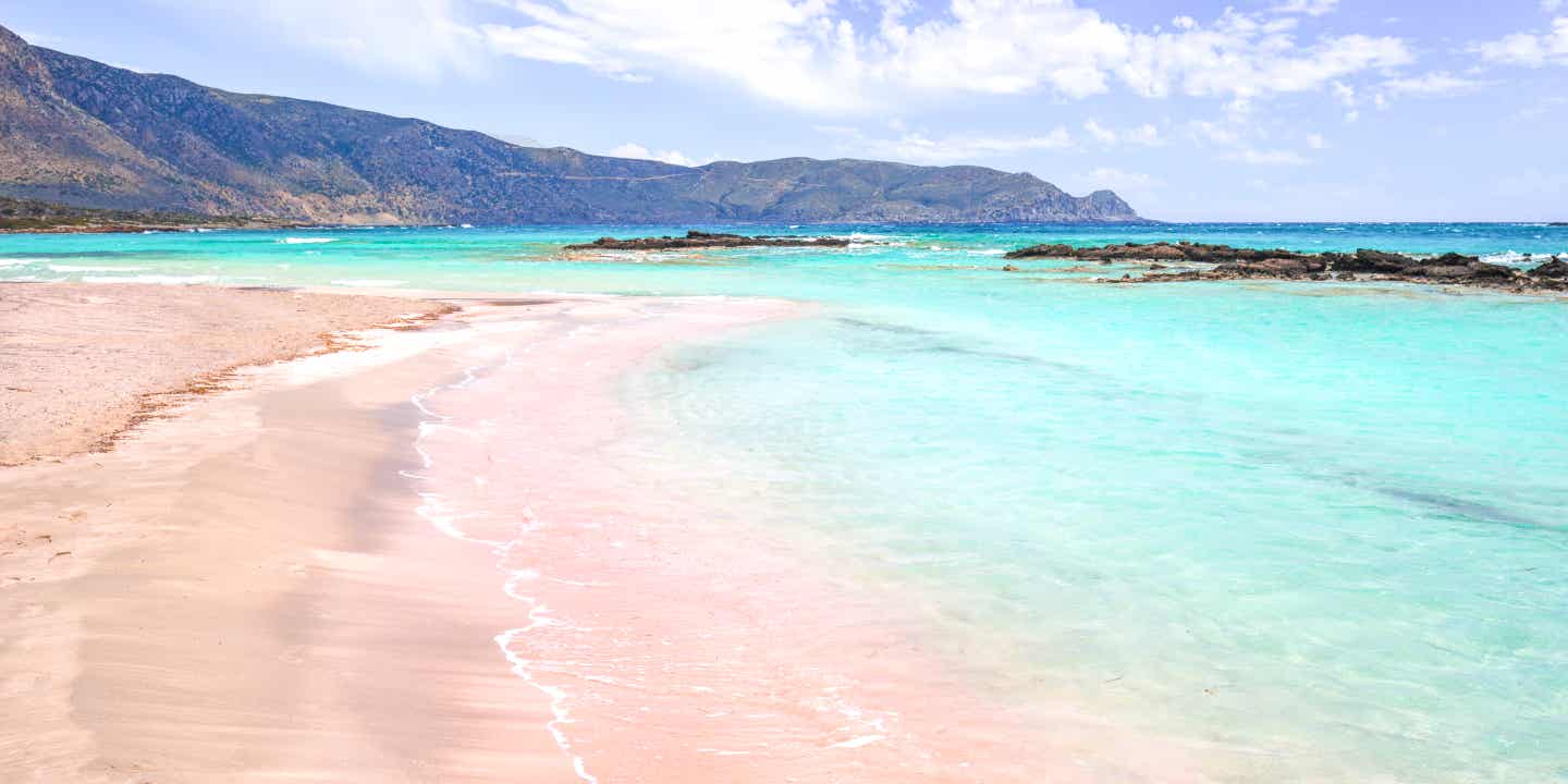 Rosa gefärbter Sand und türkiser Wasser am Elafonissi Beach auf Kreta, im Hintergrund eine Hügelkette