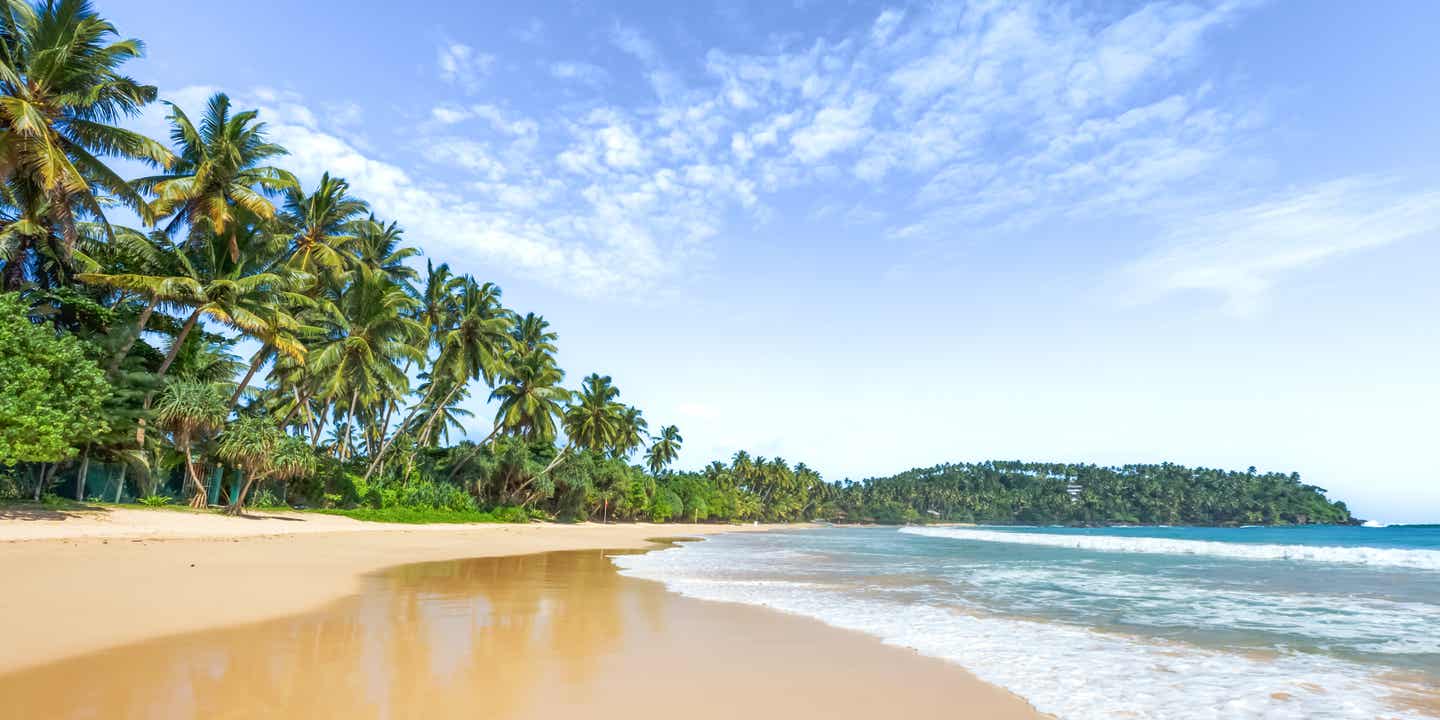 Strand mit blauem Himmel und Palmen, Wellen brechen sich am Sandstrand