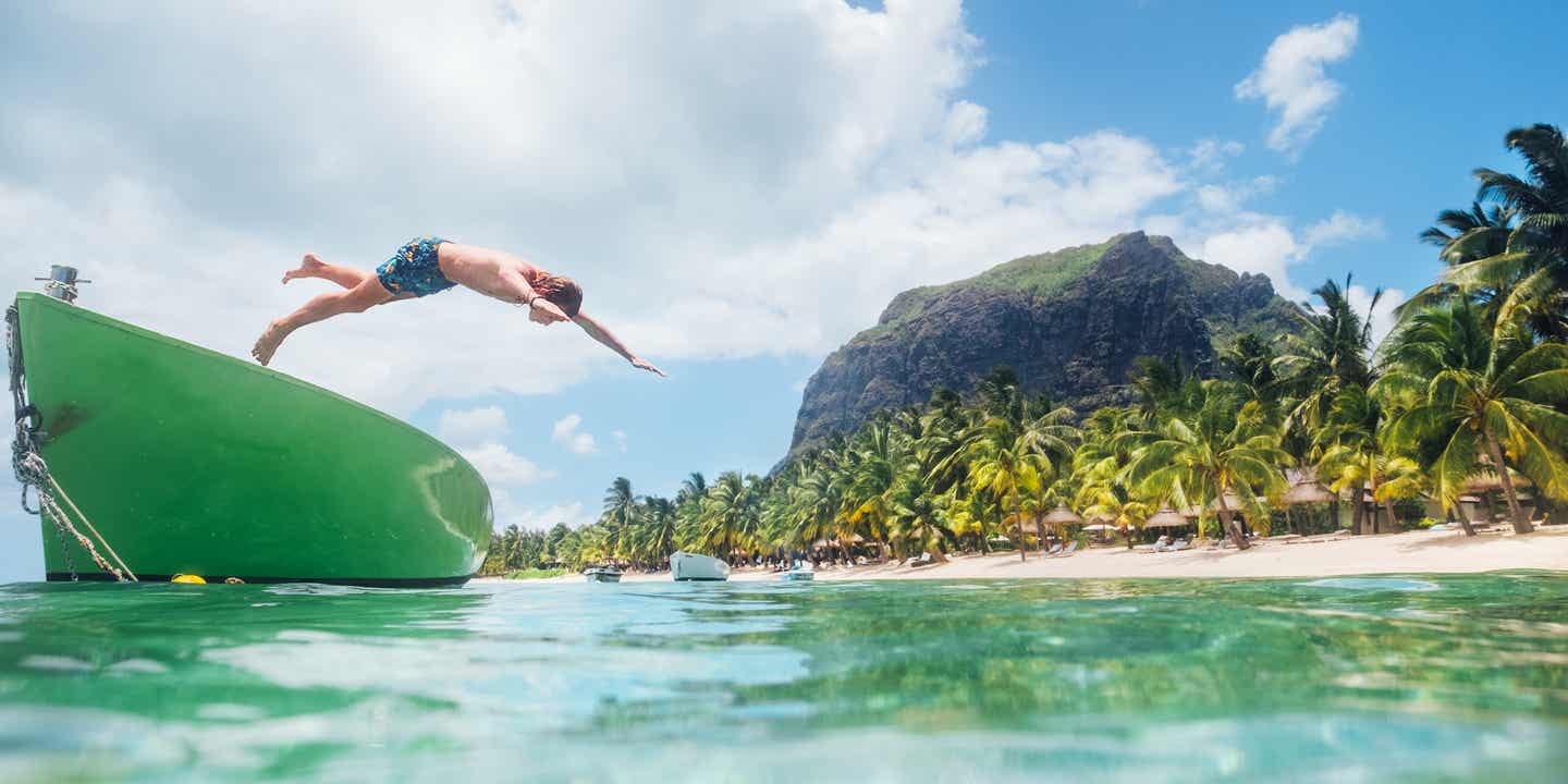 Teenager springt von einem Boot ins klare Wasser vor dem Le Morne Brabant auf Mauritius