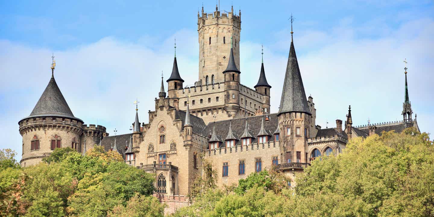 Schloss von Weitem fotografiert zwischen grünen Bäumen und blauem Himmel