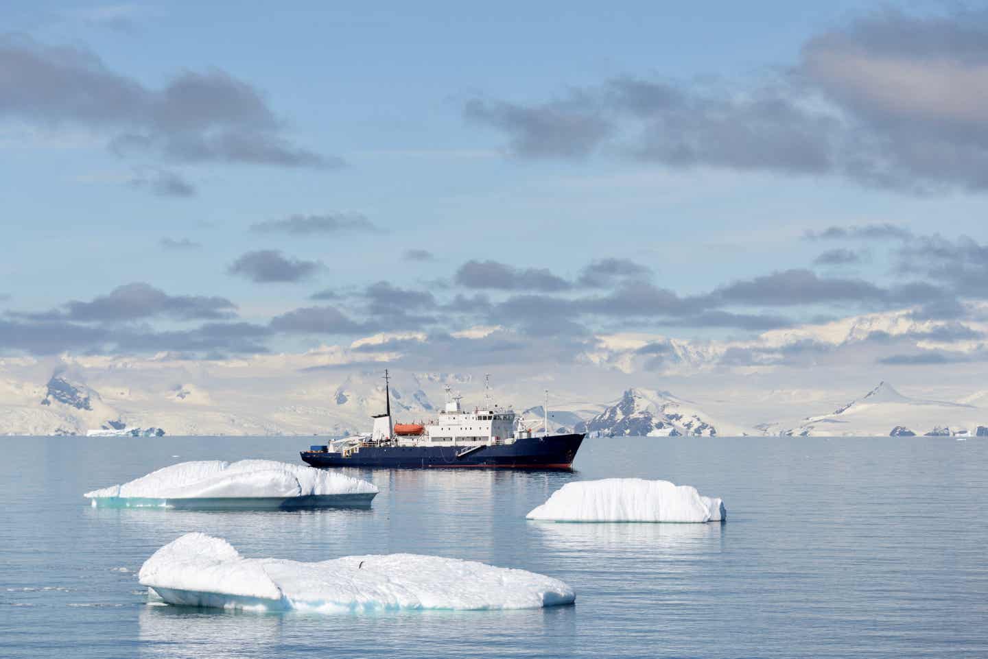 Ein Expeditionsschiff in der Antarktis; im Vordergrund ein paar Eisschollen, im Hintergrund das schneeüberzogene Festland