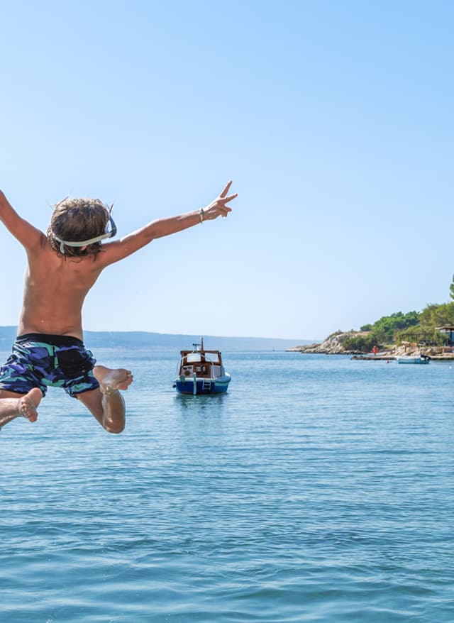 Reiseziele mit Kindern Reiseziele mit Kindern: Junge springt an einem sonnigen Urlaubstag von einem Steg ins türkisblaue Meer von Kroatien