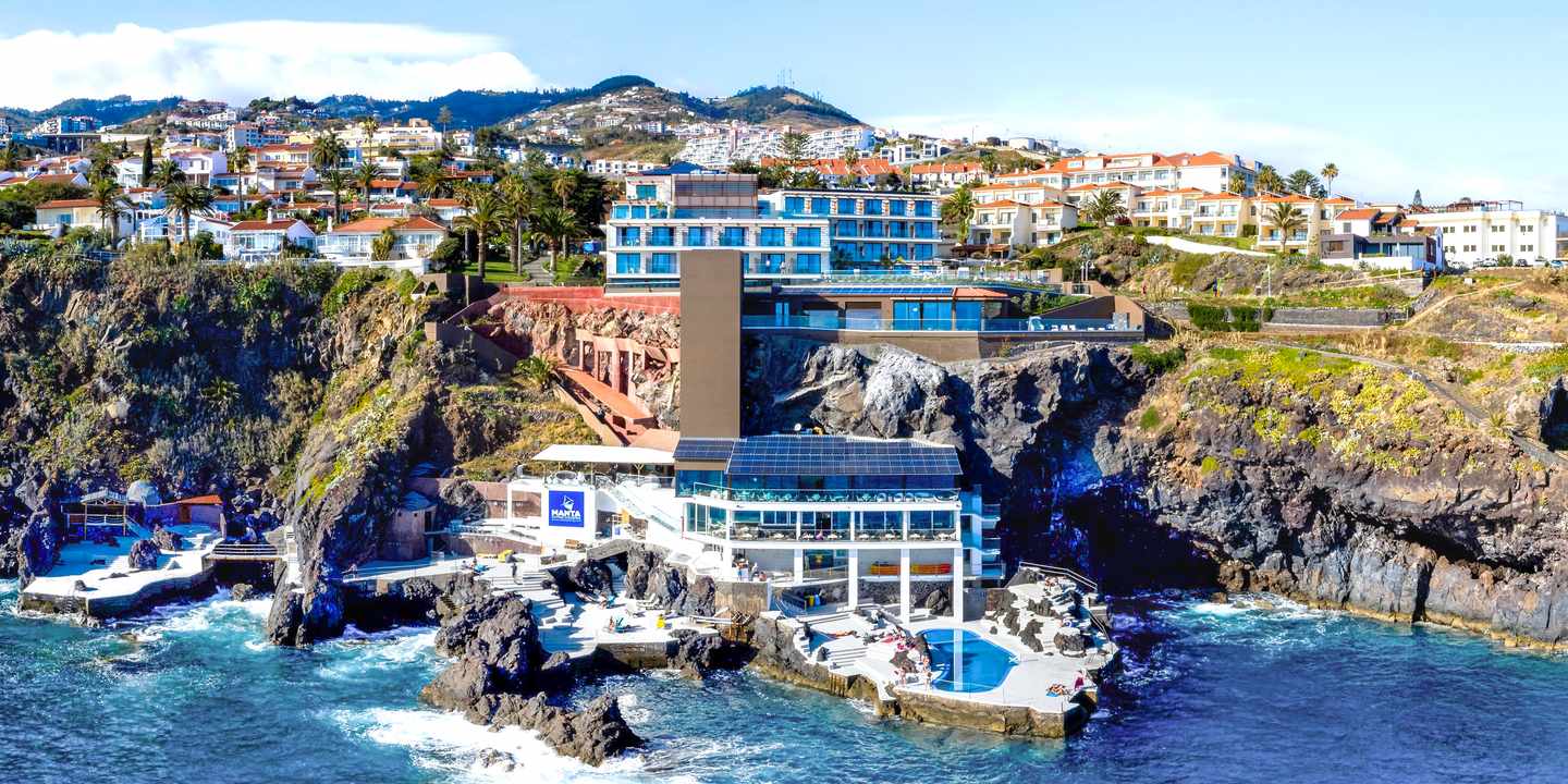 Blick vom Meer aus auf das Sentido Galomar und weitere Häuser an einer felsigen Klippe