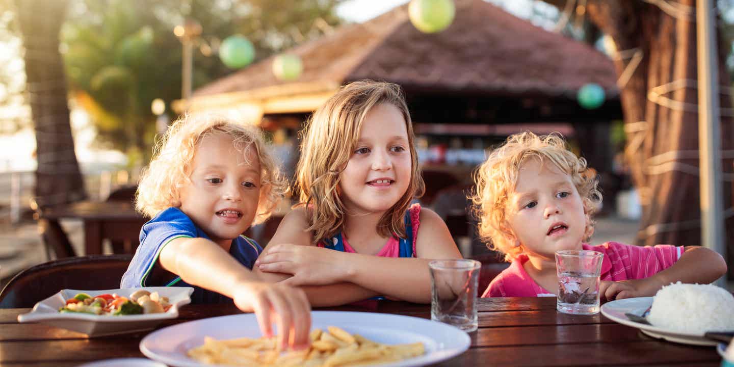 Drei Kinder essen gemeinsam in einer familienfreundlichen Sunset Bar auf Ibiza nahe der Strandpromenade