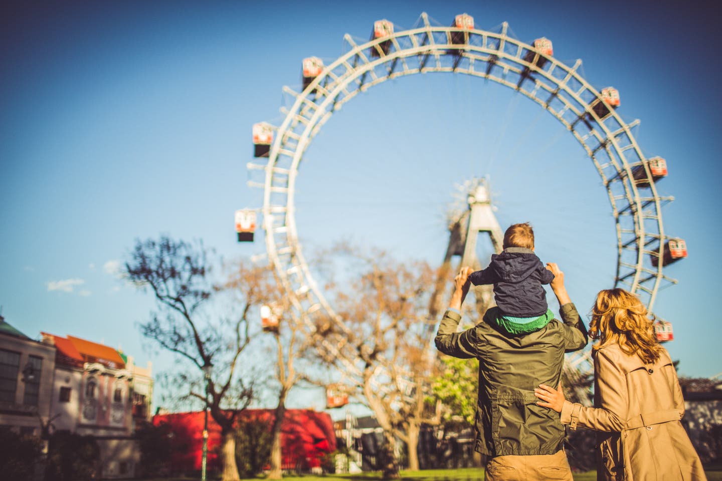 Familie von hinten zu sehen schaut auf ein Riesenrad im Freizeitpark