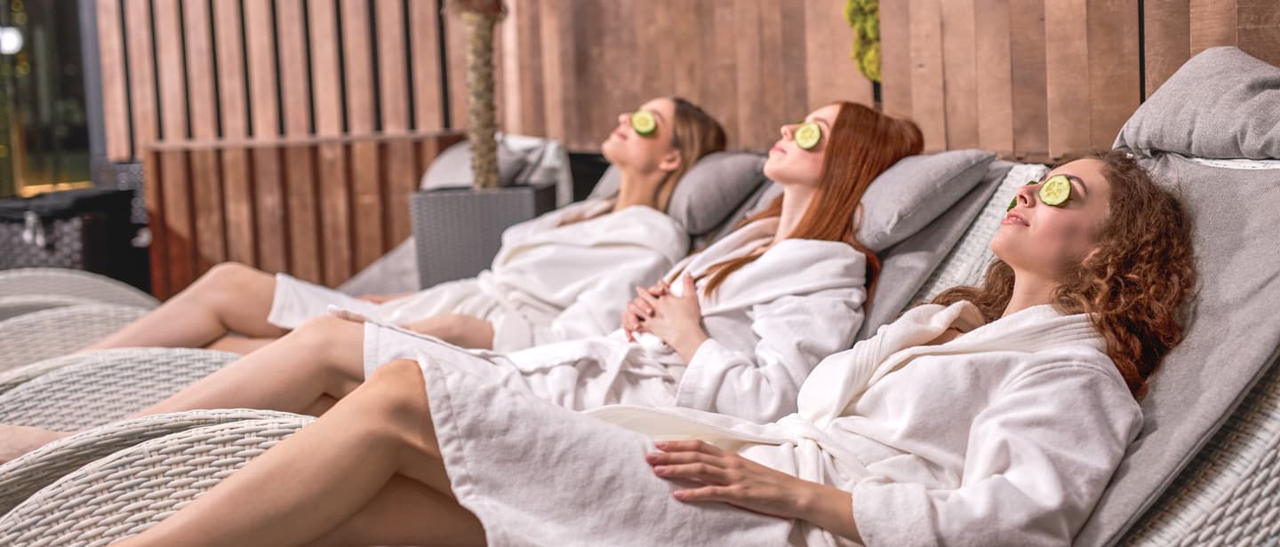Freundinnen Wellnesswochenende mit zwei Frauen im Bademantel und Gurkenscheiben auf den Augen bei einer Spa-Anwendung