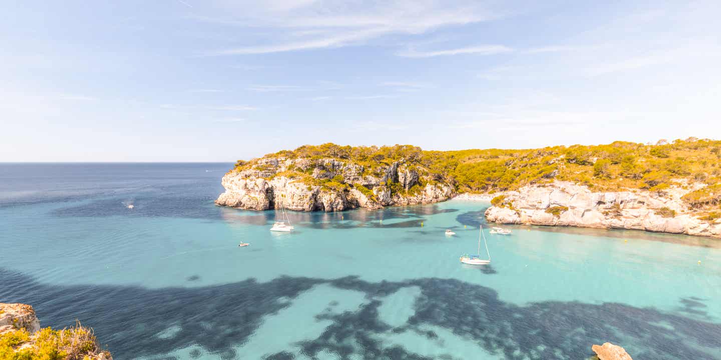 Blick auf eine Bucht mit steilen Klippen, im Vordergrund blaues Wasser, im Hintergrund blauer Himmel