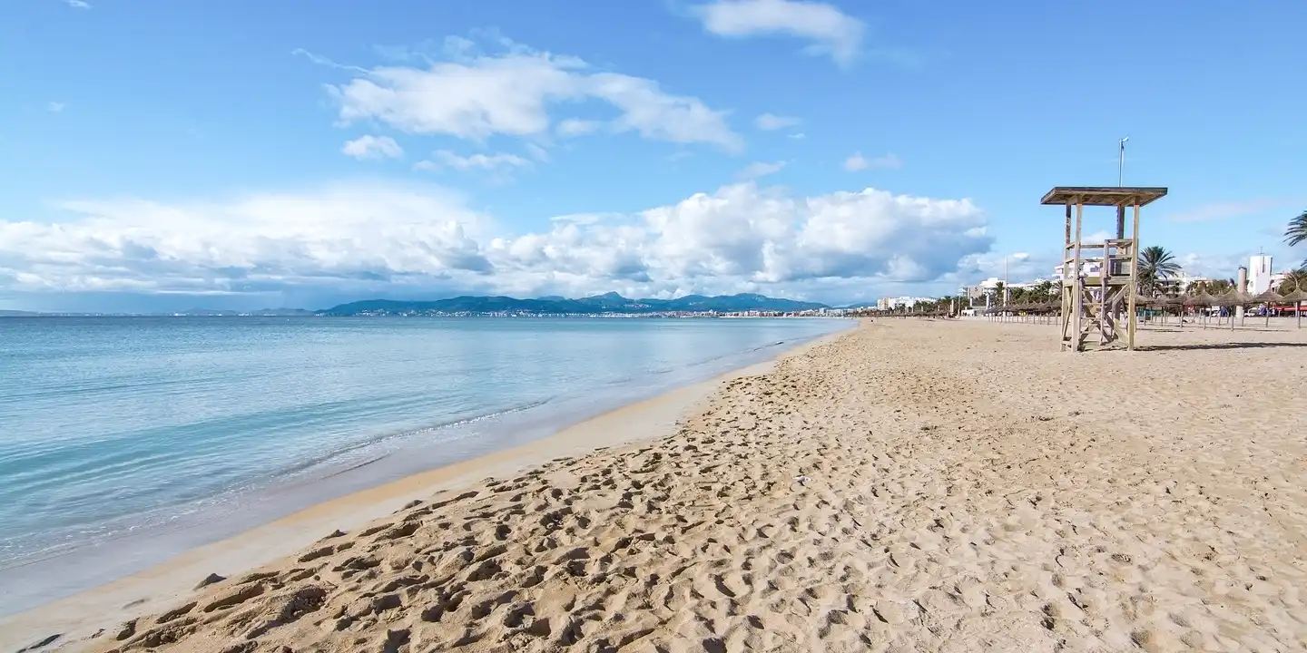 Sandstrand von Can Pastilla mit ruhigem Wasser, Rettungsturm und Blick entlang der Küste Mallorcas