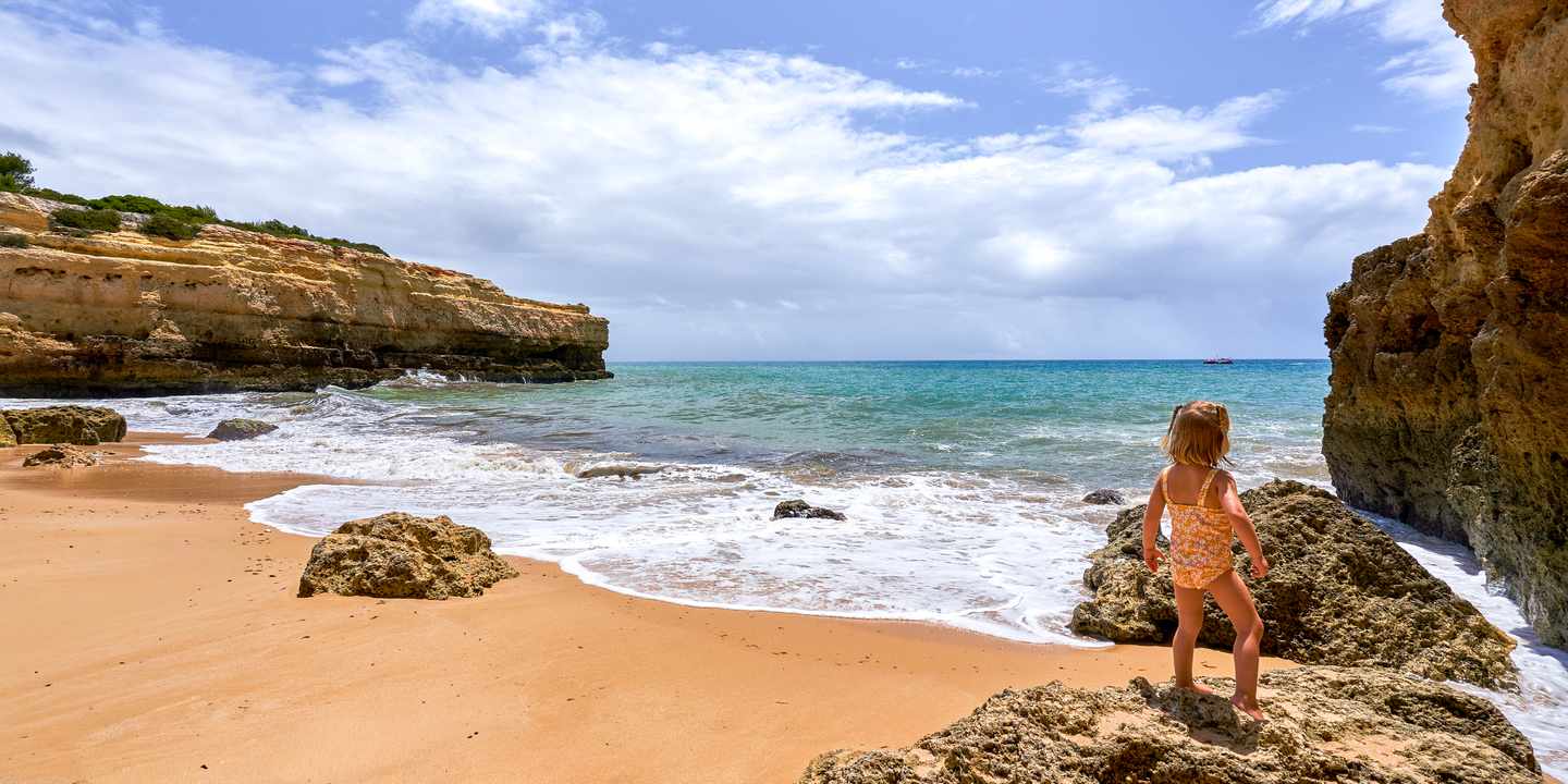 Kind steht am Strand Praia de Albandeira an der Algarveküste in Portugal mit Felsen und Meer