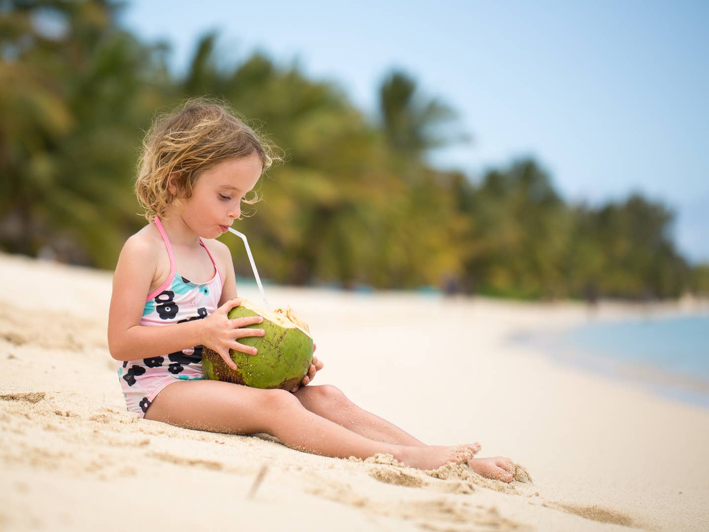  Mädchen trinkt aus Kokosnuss am Strand von Mauritius im Familienurlaub