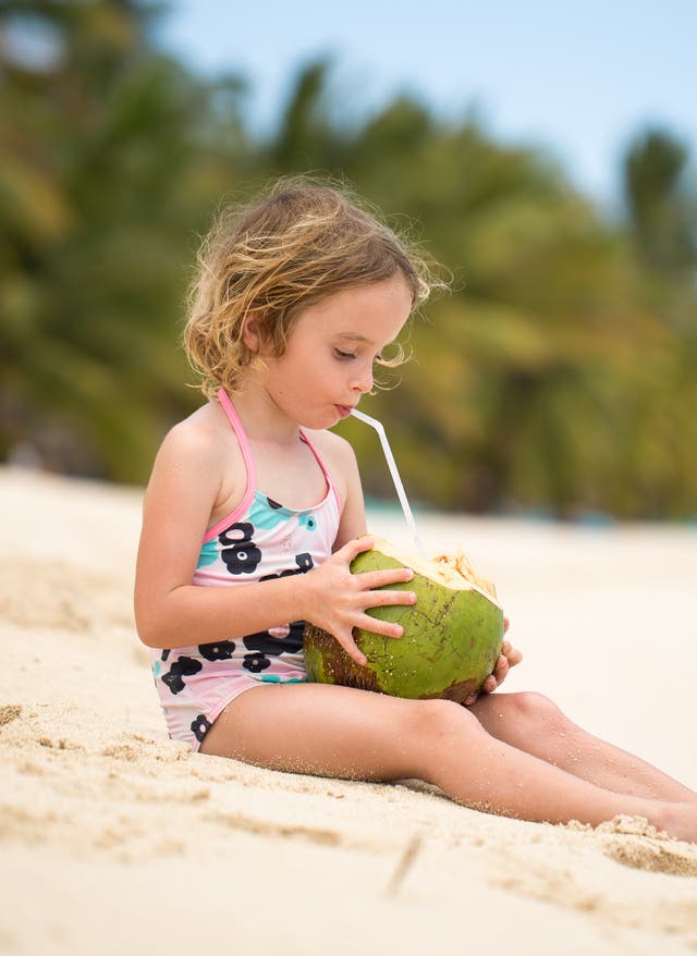 Familienurlaub Mauritius Mädchen trinkt aus Kokosnuss am Strand von Mauritius im Familienurlaub