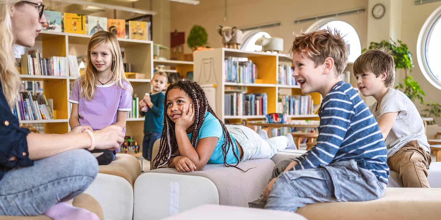 Kinder in einer Bibliothek, die einer Erwachsenen beim Lesen zuhören