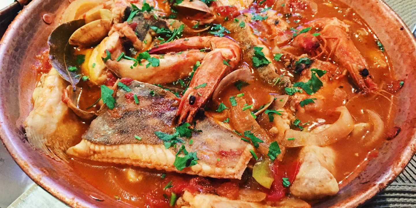 Cataplana mit Fisch, Garnelen und Muscheln in würziger Tomatensauce in traditionellem Topf
