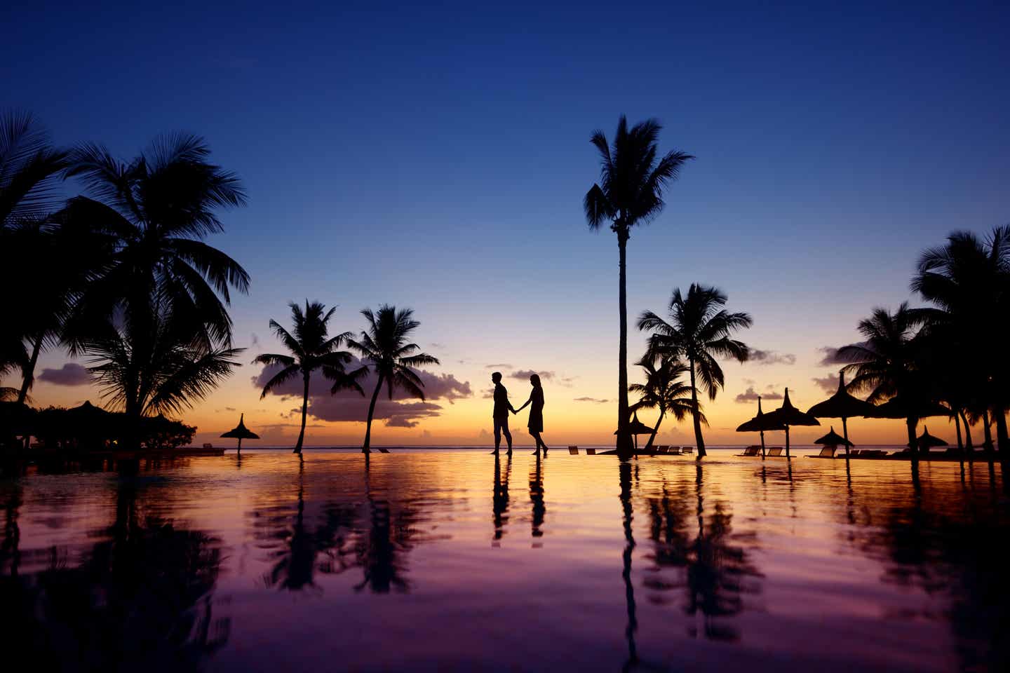 Ein Paar spaziert bei Sonnenuntergang eine mit Palmen bewachsene Hotelanlage entlang