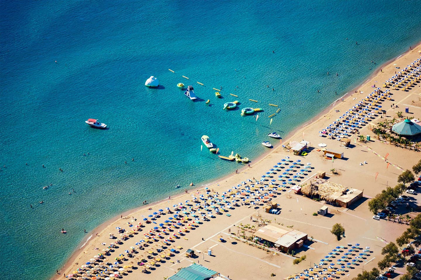 Sandstrand am Tsambika Beach auf Rhodos mit Sonnenschirmen, Liegen und Booten im Meer